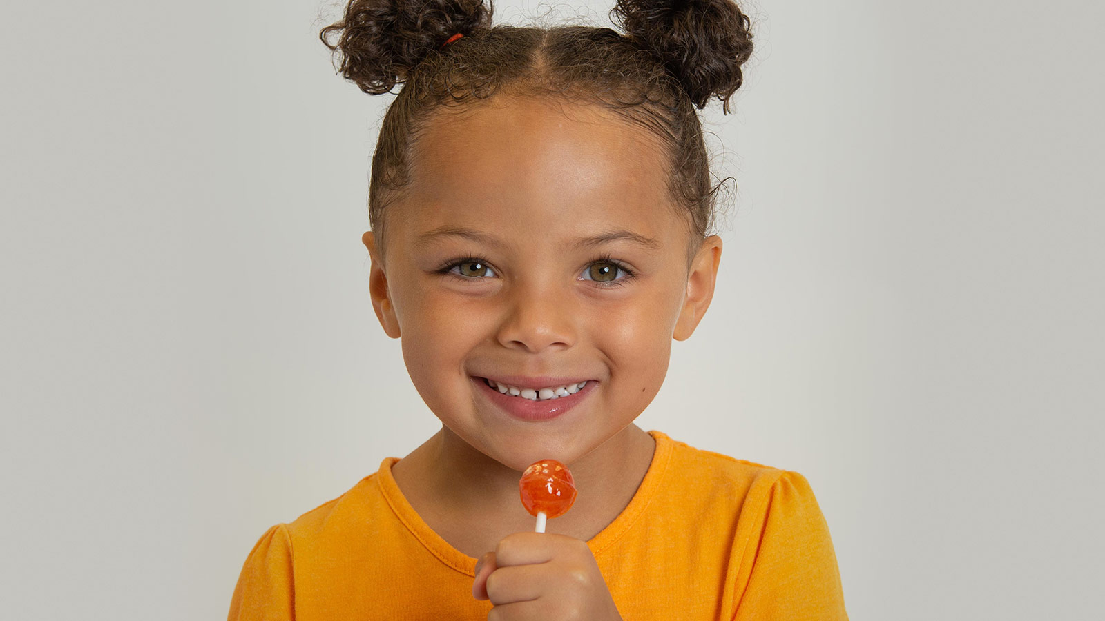 A little girl holds an orange lollipop
