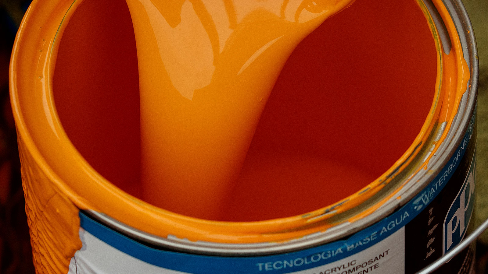 orange paint being poured into a paint can