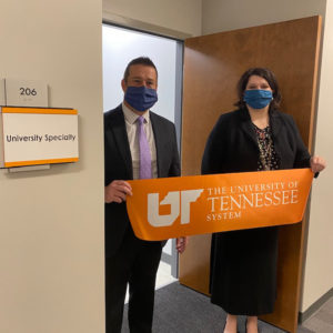 Two medical professionals in face masks hold an orange ribbon with the UT System logo in front of an office suite