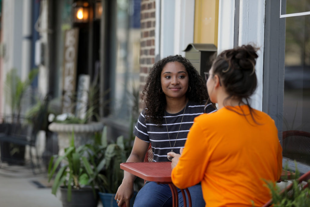 Two women talk outside at a cafe table