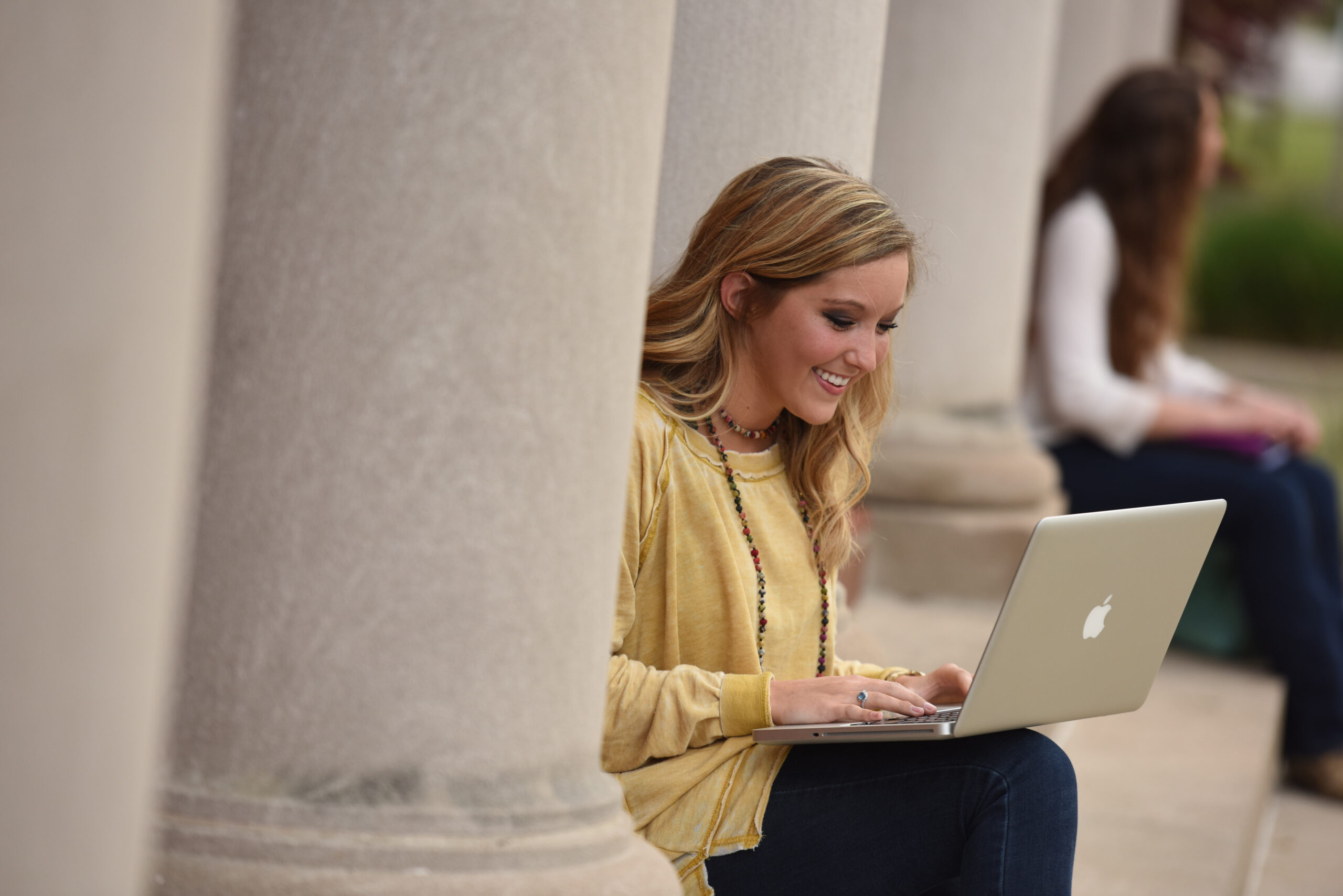 Student in a yellow shirt typing on her laptop while smiling.