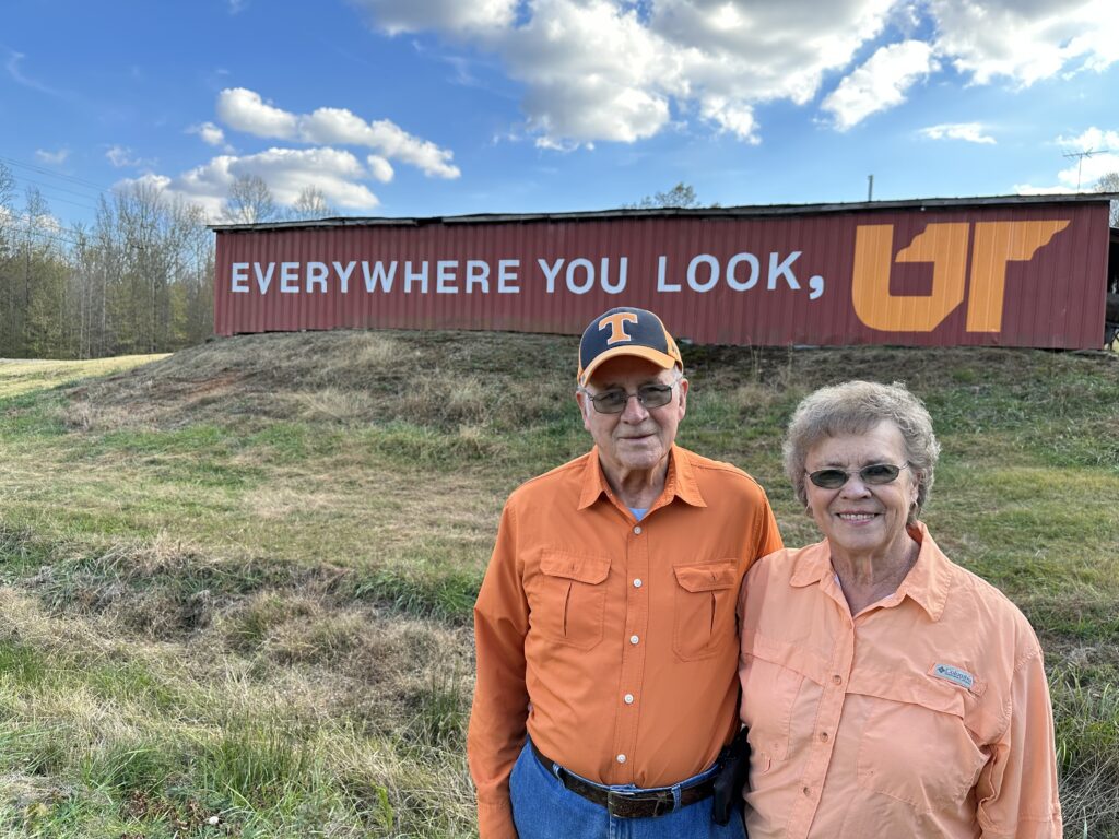 UT alumni Charles and Joyce McBride pose in front of their red barn featuring an orange and white Everywhere You Look, UT mural in Lexington, Tennessee